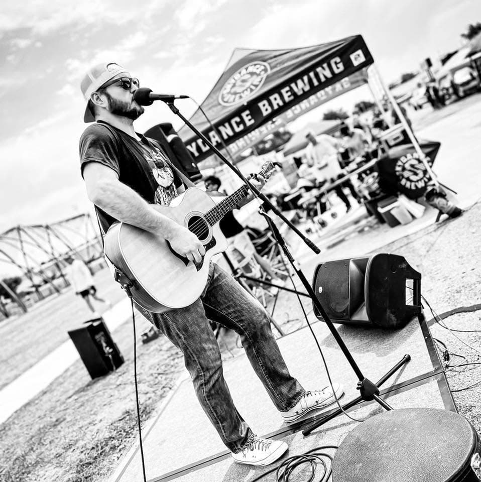 Nate Kelley singing and playing acoustic guitar at an outdoor performance