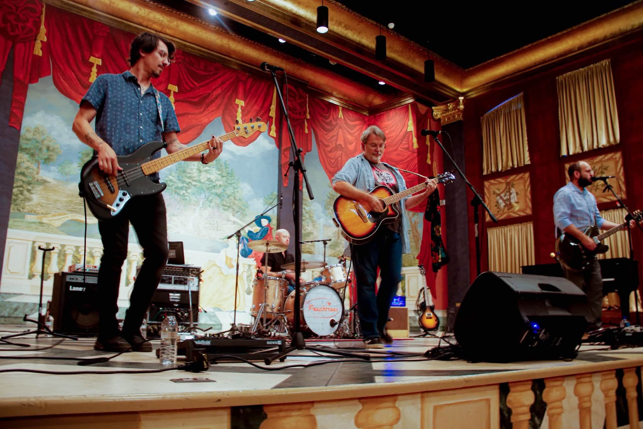 The Peach Trees performing beneath red curtains on the Enid Symphony Hall stage